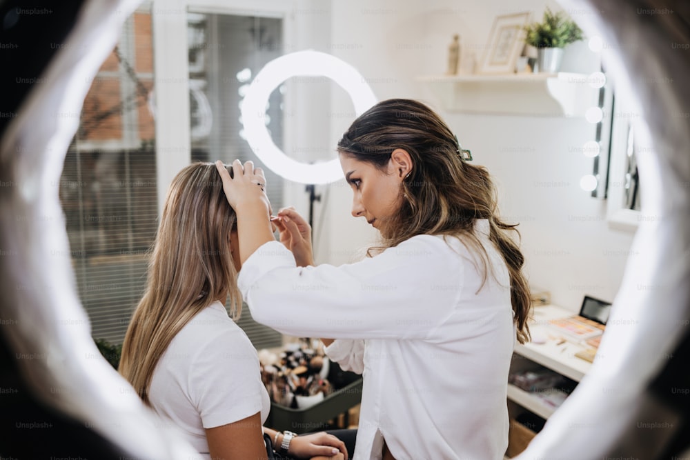 Makeup process. Professional artist applying make up on model face. Close up portrait of beautiful blonde woman in beauty saloon.