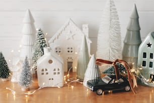 Frohe Weihnachten und einen guten Rutsch ins neue Jahr! Festliche Weihnachtsszene, Miniatur-Feriendorf.  Stilvolles Auto mit Weihnachtsbaum, Häuschen und verschneiten Bäumen auf weißem Hintergrund. Weihnachtshintergrund