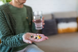 Cropped view of sick and ill mature aged woman holding different pills on palm hand, showing medical preparat on camera