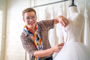 아시아 LGBTQ 남자 신부 가게 주인이 웨딩 스튜디오의 탈의실에서 마네킹을 바느질하여 웨딩 드레스를 측정하는 줄자를 사용하는 초상화. 중소 기업 기업가 웨딩 플래너 및 재단사 디자이너 개념