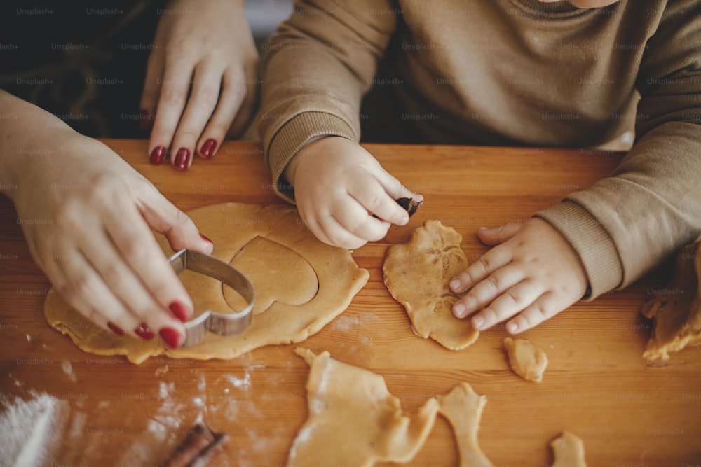 귀여운 딸과 어머니가 지저분한 테이블에 크리스마스 쿠키를 함께 만들고 있다. 진저브레드 쿠키를 위해 반죽을 자르는 엄마와 함께 사랑스러운 유아 소녀. 분위기 있는 휴가 시간. 함께 가족