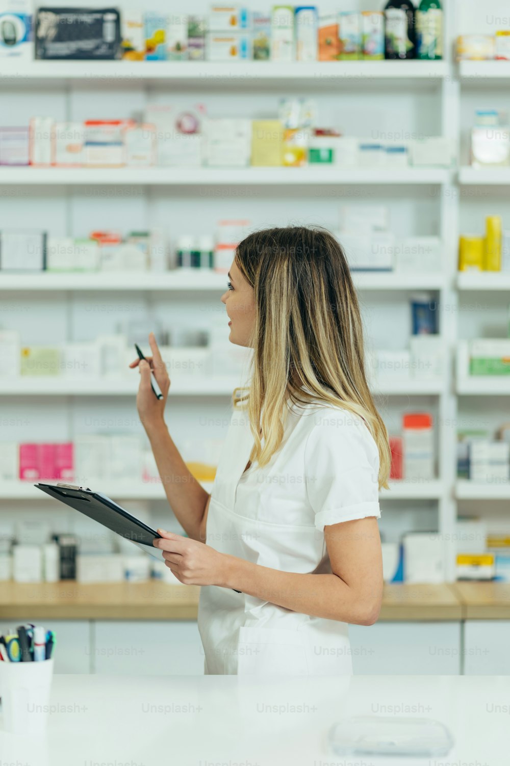 Beautiful female pharmacist working in a pharmacy while checking medications on the shelf