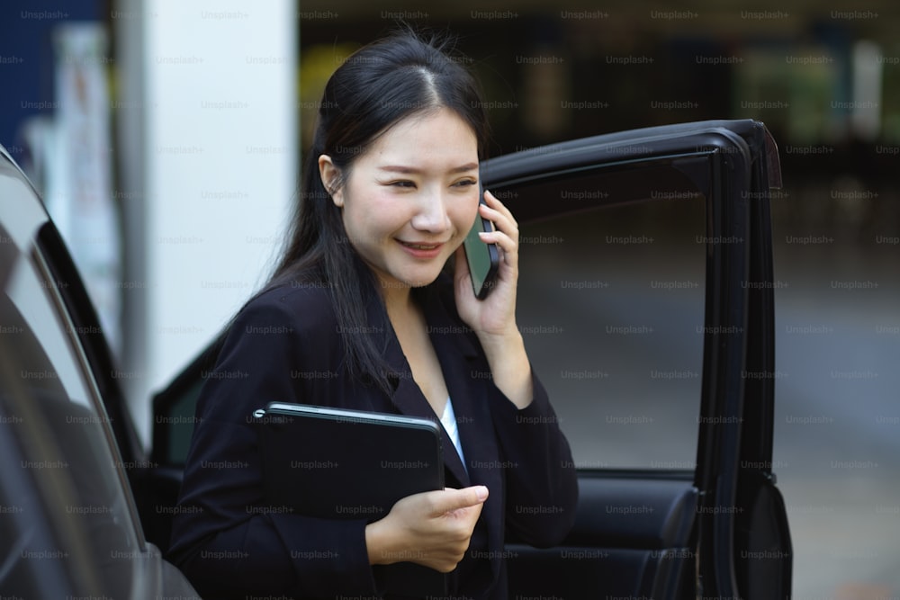 Eine selbstbewusste Managerin telefoniert, während sie aus ihrem Auto steigt. Businesswoman Konzept.