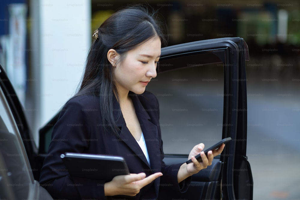 바쁜 아시아 사업가가 택시에서 내리면서 조수에게 스마트폰 문자 메시지를 사용합니다.