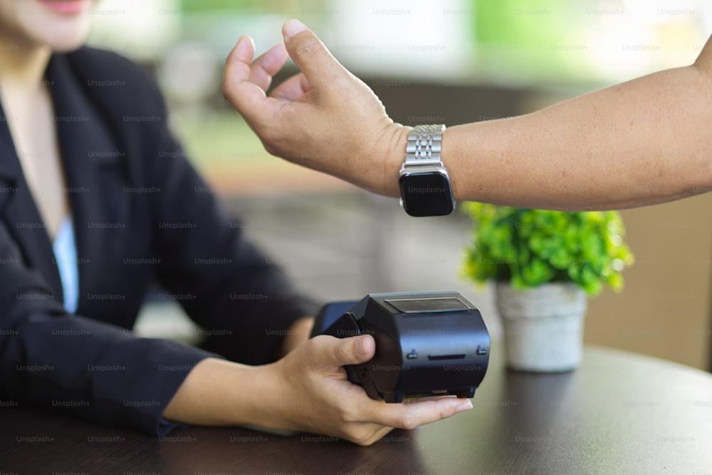 Image recadrée d’un homme utilisant sa smartwatch moderne pour payer des paiements en ligne avec un terminal de paiement.