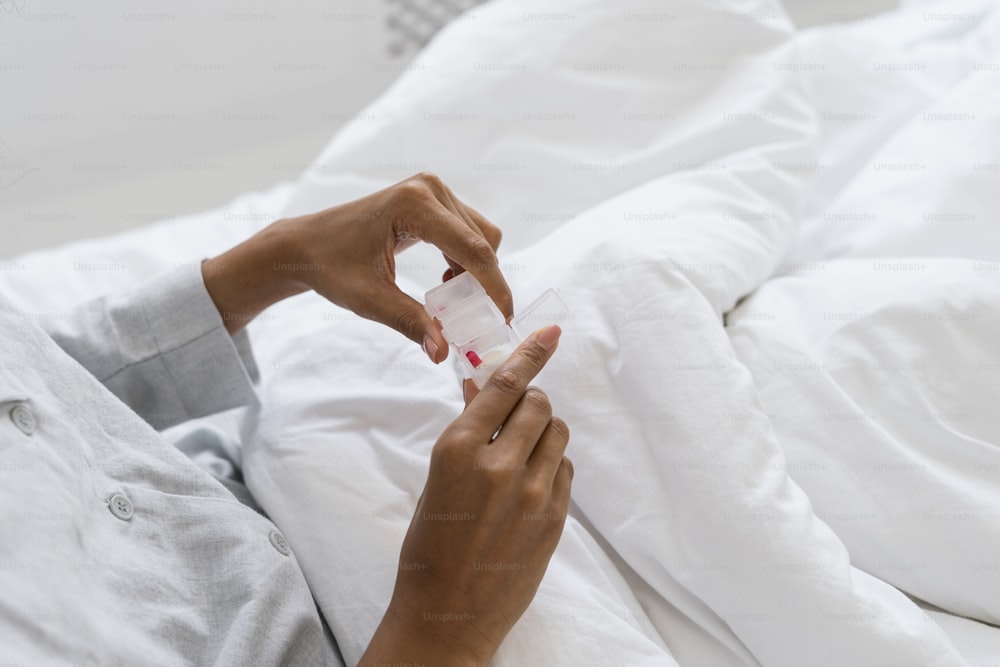 손에 알약이 든 상자를 들고 침대에 앉아 잠옷을 입고 있는 아프리카계 미국인 여성의 자른 모습. 집에서 약을 복용하는 아픈 여성. 의료, 건강 문제 개념