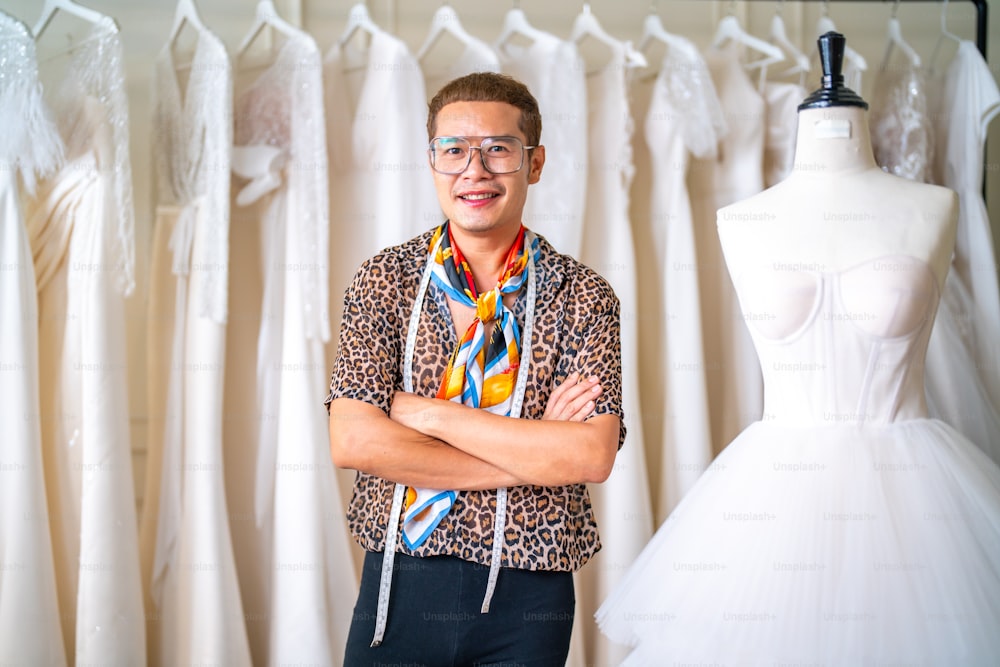 Retrato do proprietário da loja de noivas LGBTQ asiático usando fita métrica medindo vestido de noiva no manequim de costura no provador do estúdio de casamento. Empreendedor de pequenas empresas planejador de casamentos e conceito de designer de alfaiataria