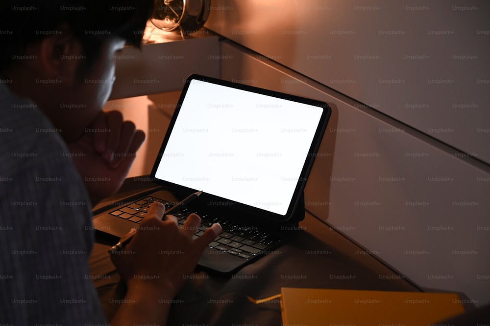 늦은 밤에 침대에 누워 컴퓨터 태블릿으로 일하는 청년.