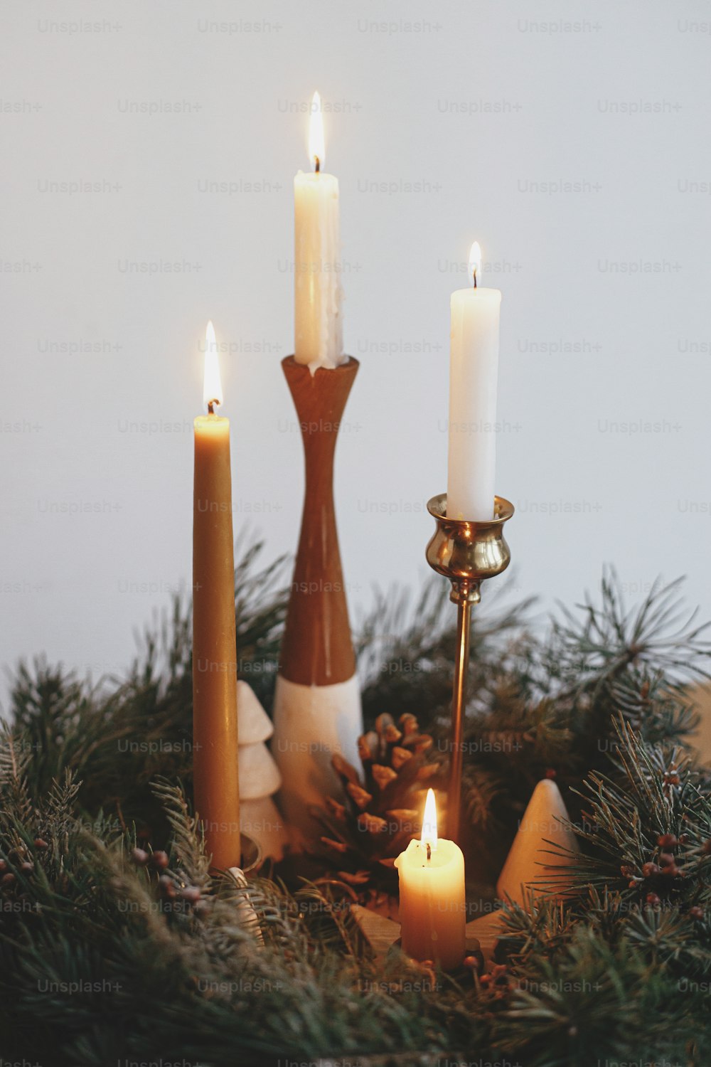 Stylish candles burning in christmas wreath with pine cones and tree decor on wooden table on background of white wall in modern festive room. Christmas advent. Atmospheric winter holidays time