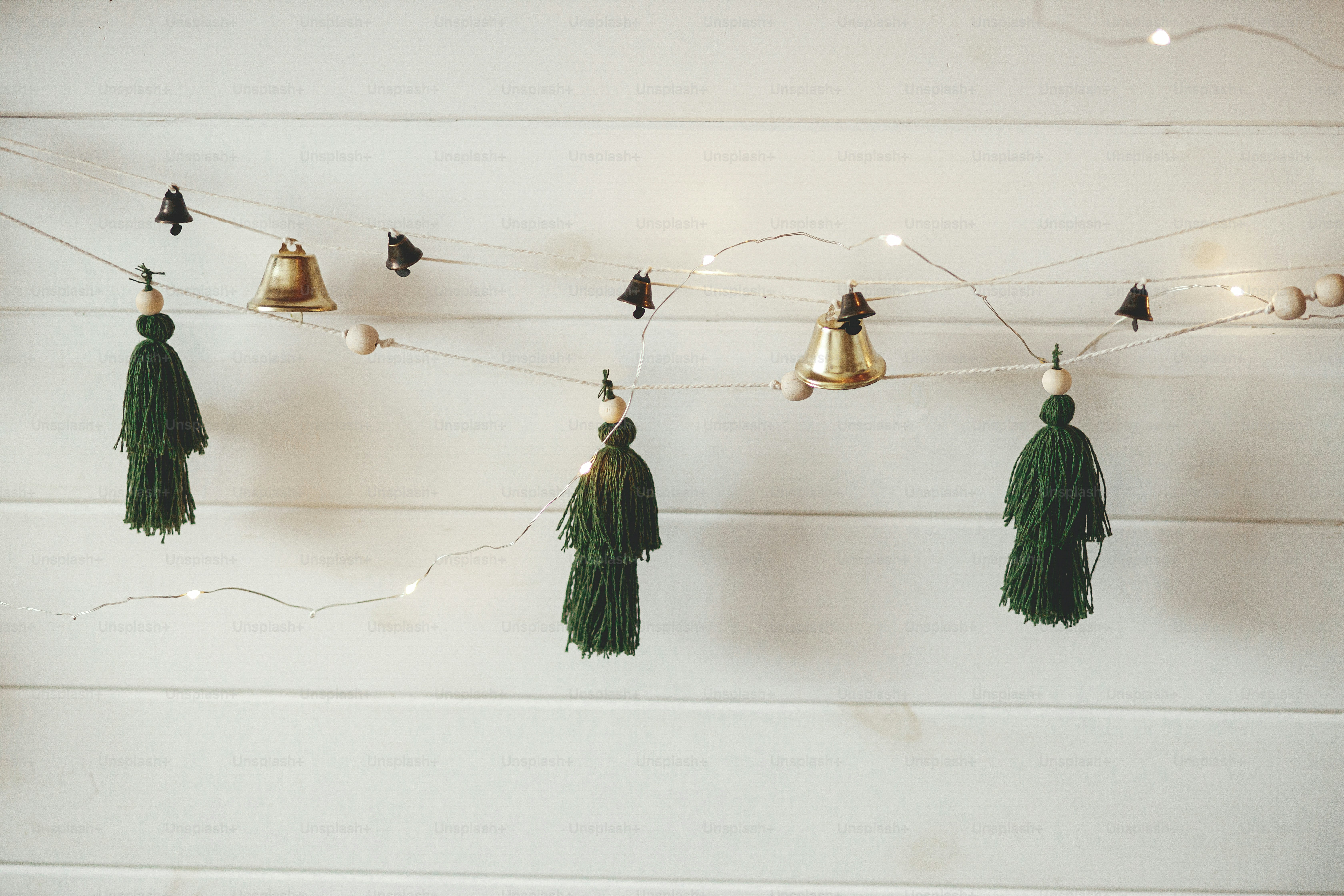 Guirlanda de Natal elegante com pinheiros de linha feitos à mão e sinos na parede de madeira branca com luzes de Natal. Sala escandinava atmosférica decorada festivamente. Decorações Boho