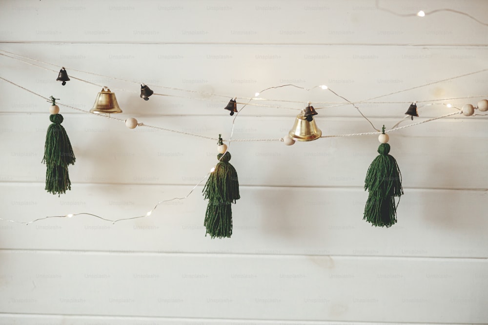 Elegante ghirlanda di Natale con pini filettati fatti a mano e campane su parete di legno bianco con luci di Natale. Camera scandinava d'atmosfera decorata a festa. Decorazioni boho