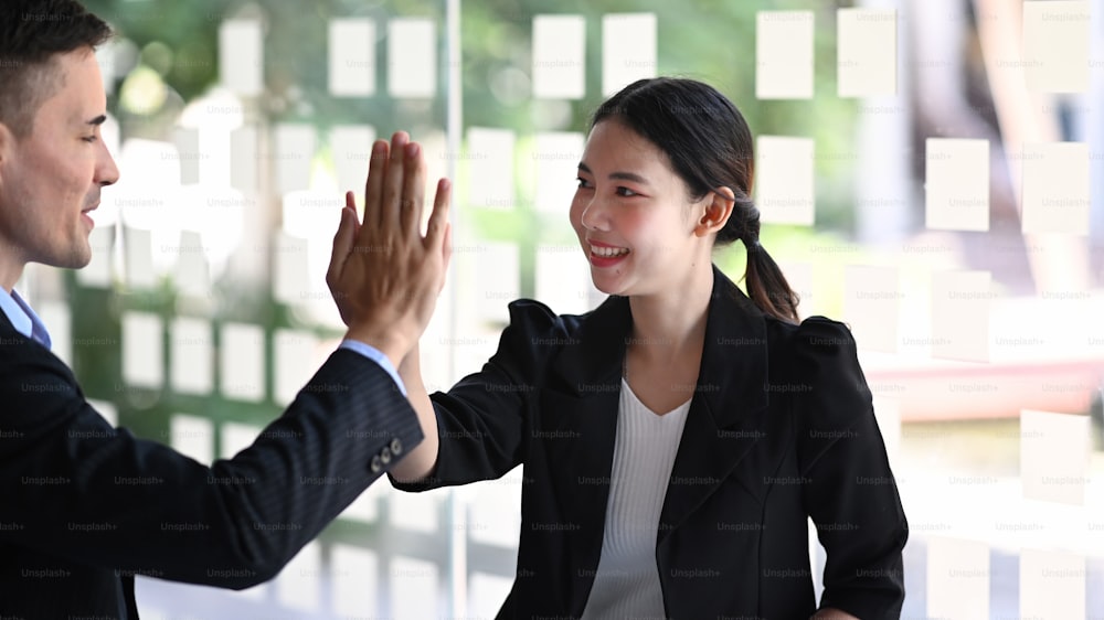 Happy young businesswoman giving high five with her colleagues for celebrating successful project.