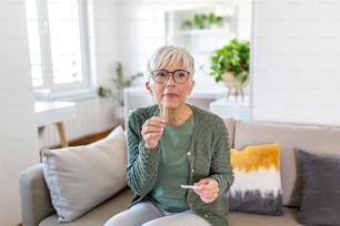 Mature woman taking a Self-swabbing home tests for COVID-19 at home with Antigen kit. Introducing nasal stick to check the infection of Coronavirus. Quarantine, pandemic.