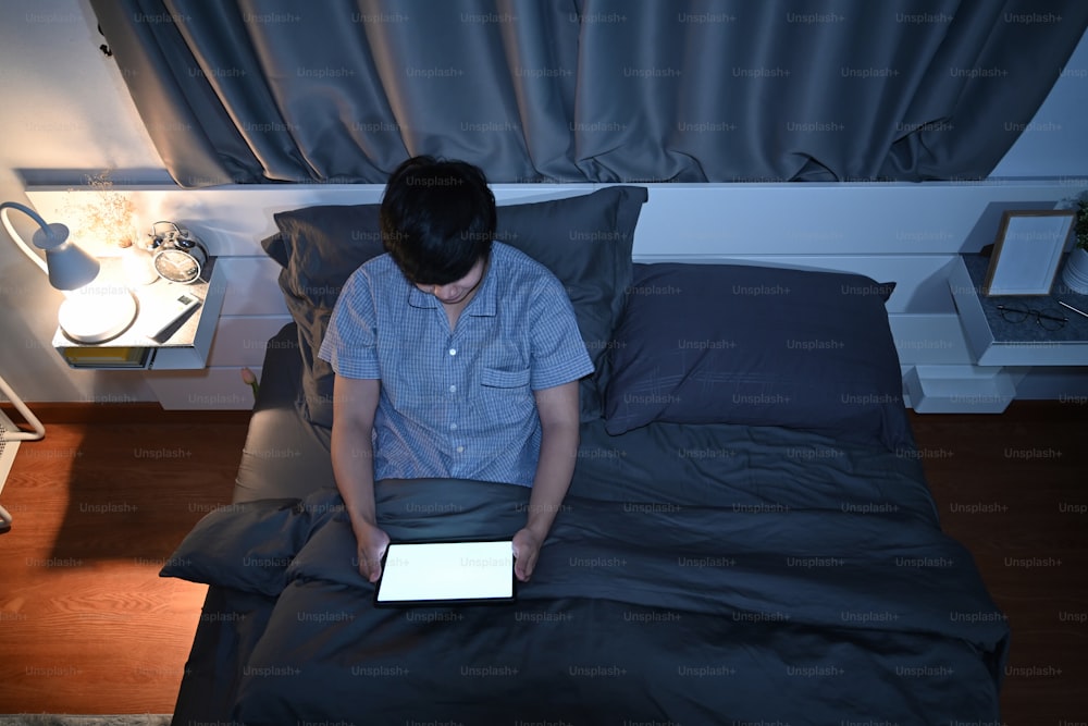 Overhead view man siting in bed and using digital table at night.