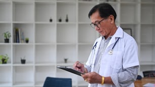 Mature doctor in white uniform working in medical office.