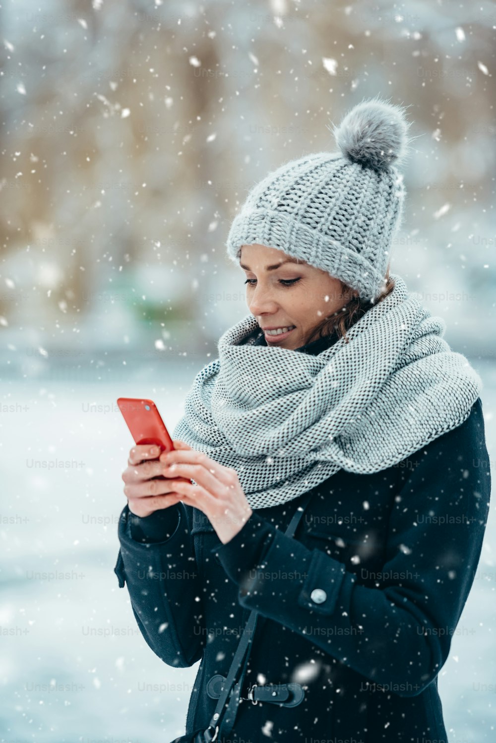 Hermosa mujer joven usando teléfono inteligente y usando bufanda y un sombrero en un frío día de invierno durante la nieve