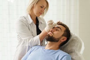 Médico femenino y cliente masculino durante las inyecciones de relleno en una clínica de medicina estética