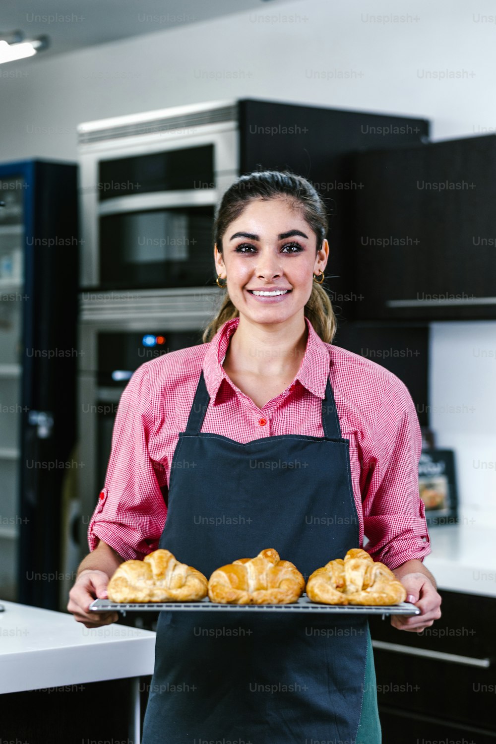 멕시코 라틴 아메리카의 부엌에서 오븐에서 크로와상을 굽는 젊은 라틴 여성