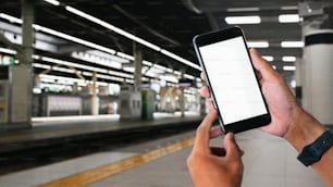 Mãos do homem segurando smartphone com fundo da estação ferroviária.