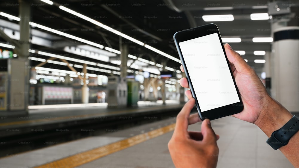 Man hands holding smartphone with railway station background.
