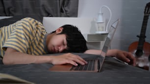 Joven asiático cansado durmiendo en la cama cerca de la computadora portátil.