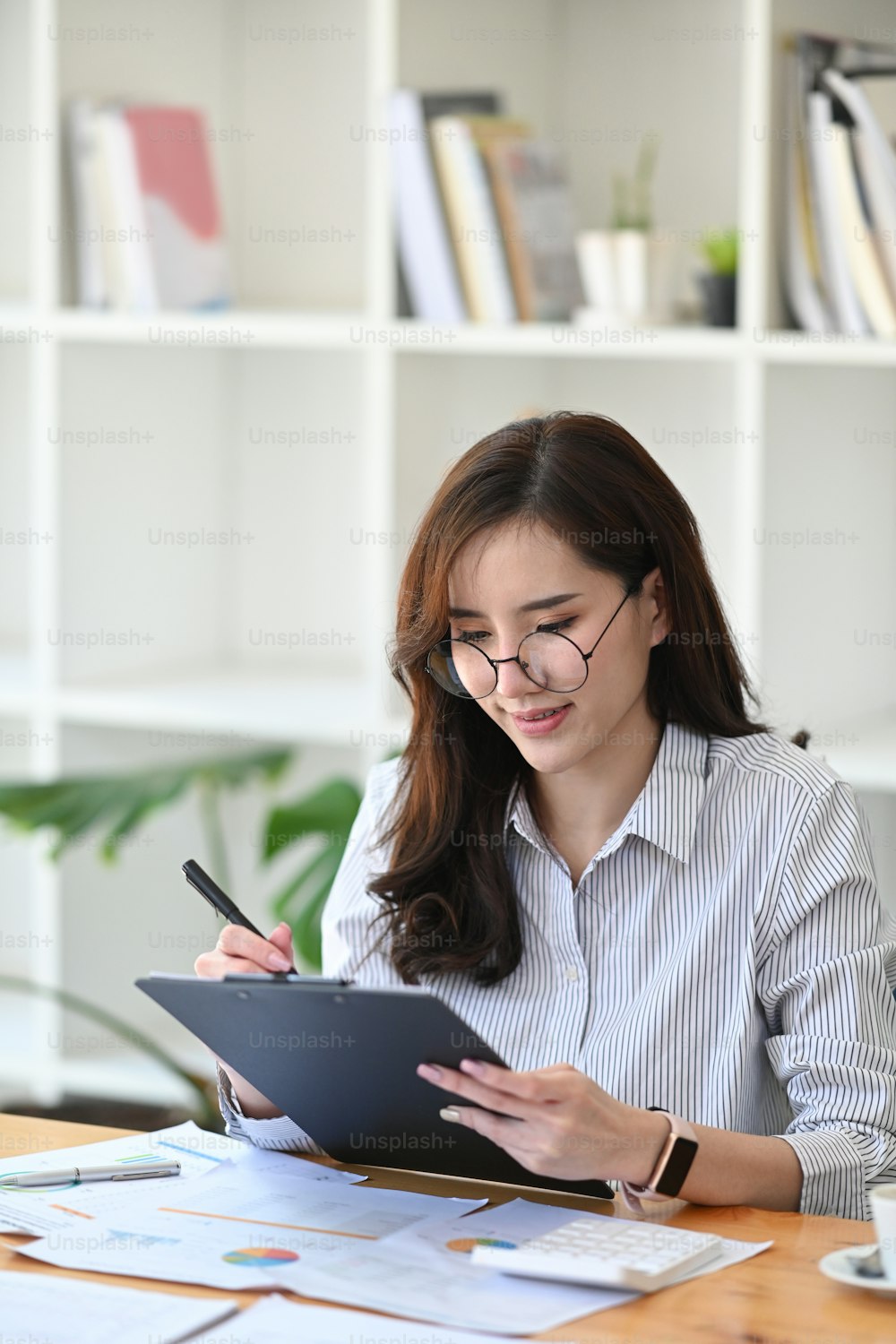 Asian businesswoman sitting in office and checking information on financial document.