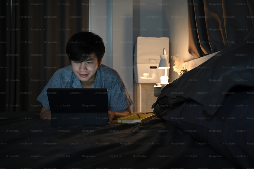 ベッドの上でパソコンのタブレットを操作している若い男性。