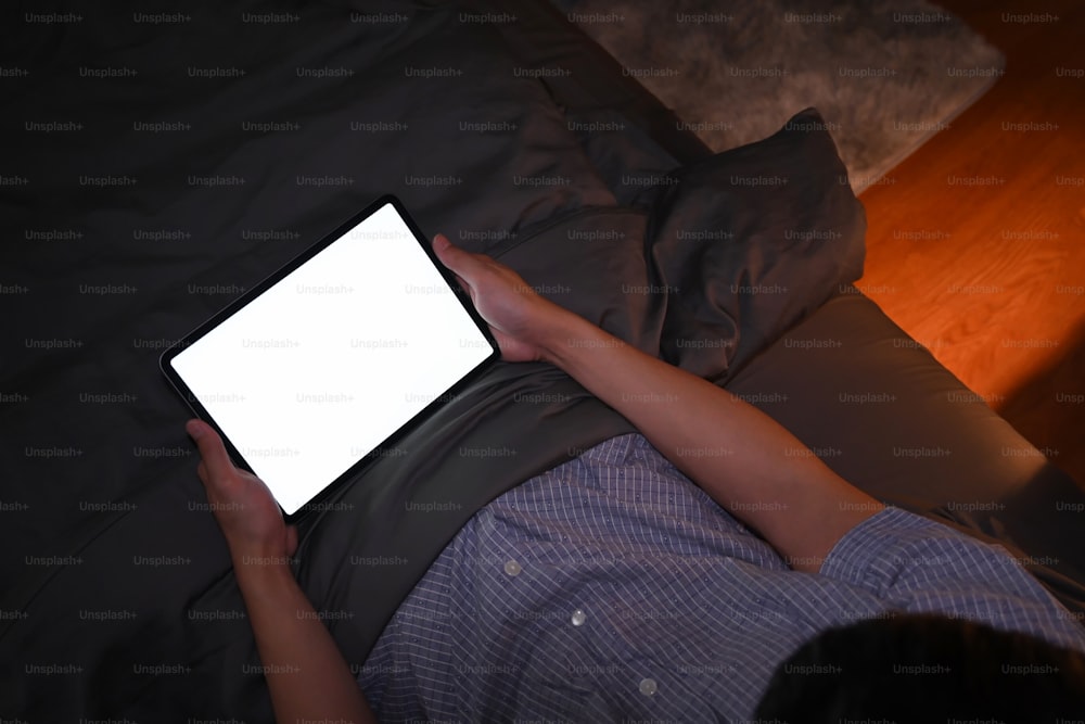 Above view asian man using digital tablet in his bed at night.