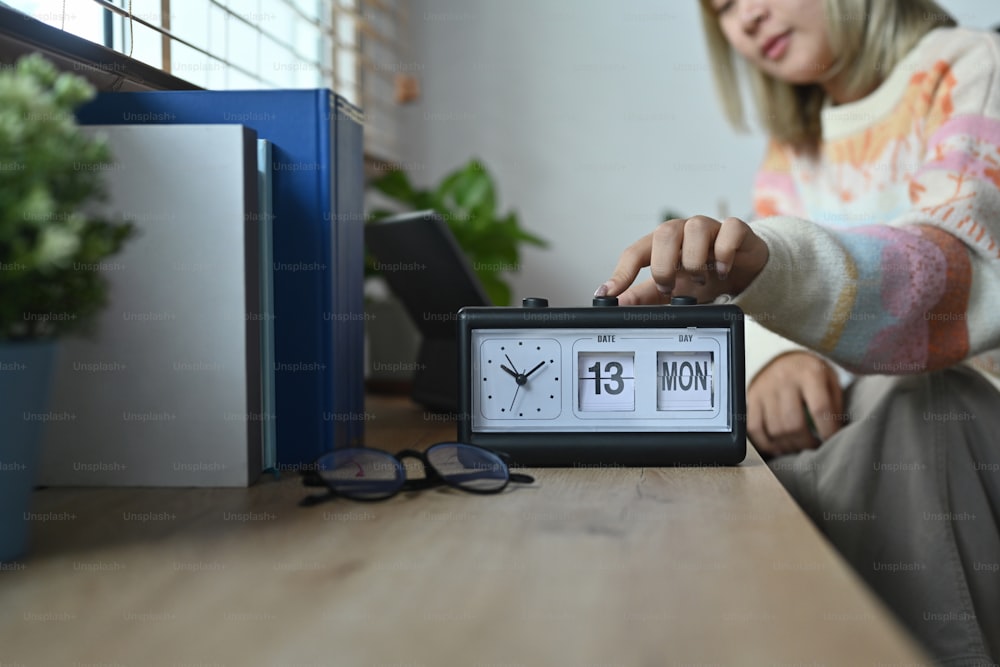 Smiling woman in warm sweater hand adjusting or changing the time on clock.