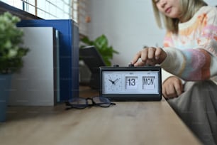 Smiling woman in warm sweater hand adjusting or changing the time on clock.