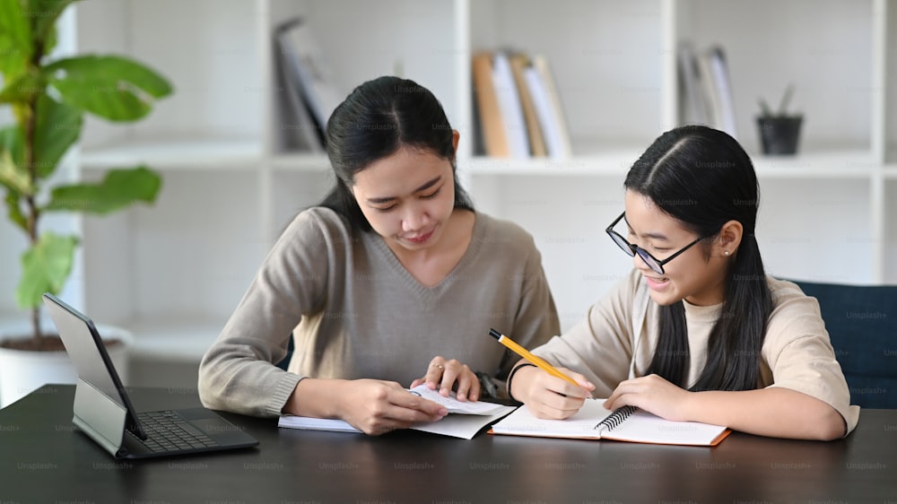 Attentive asian mother helping daughter doing homework at home.
