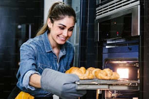 young Latin woman baking croissant on oven in kitchen in Mexico Latin America