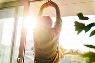 Back view of senior woman stretching in the beams of the sun