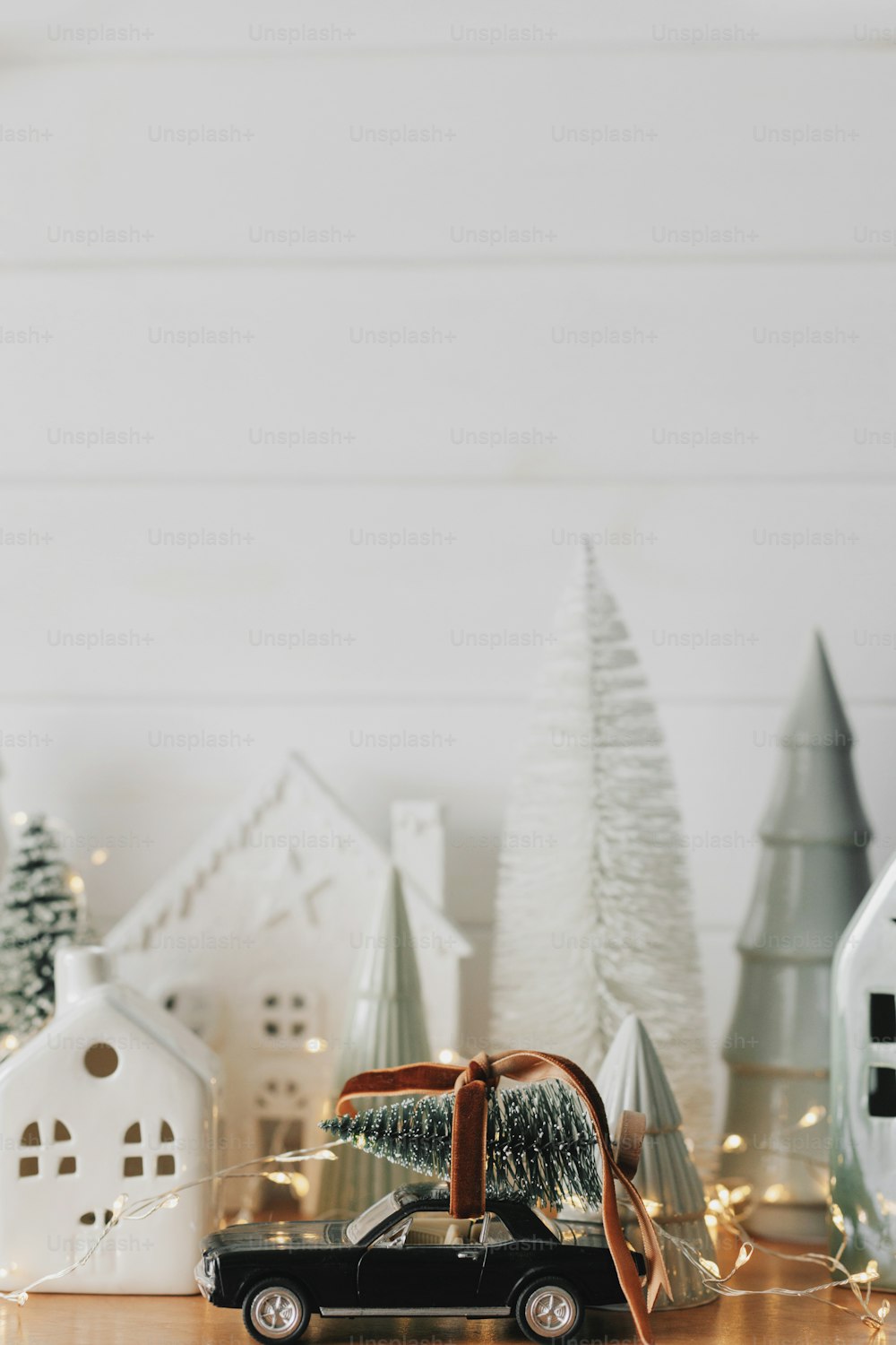 Merry Christmas and Happy New Year! Festive Christmas scene, miniature holiday village. Car with christmas tree, little houses and snowy trees on white background. Styling Christmas sideboard