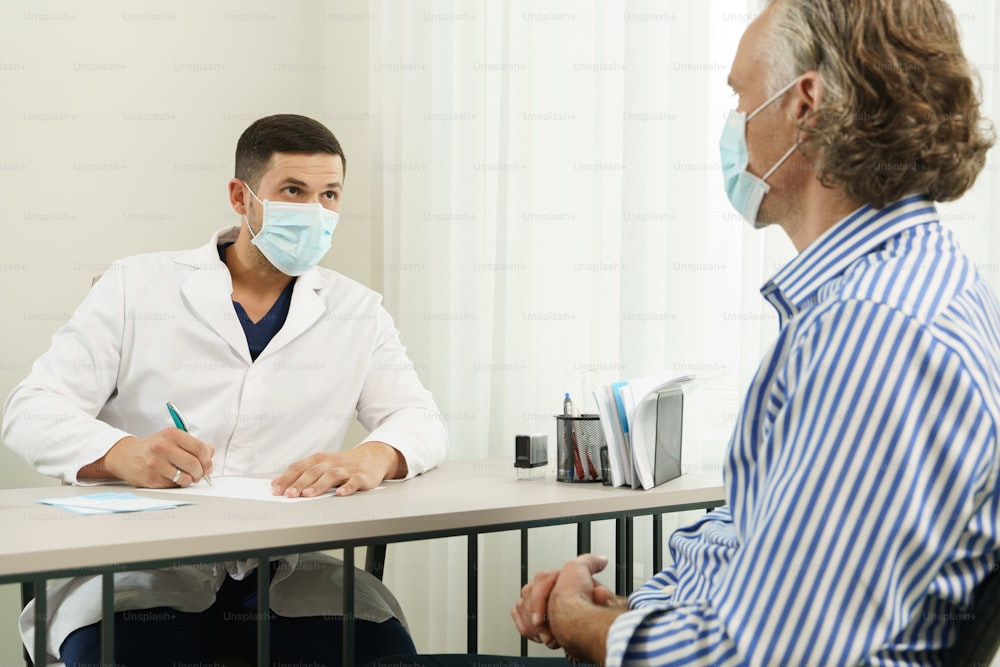 Doctor and middle aged male patient wearing prevention masks during consultation in office
