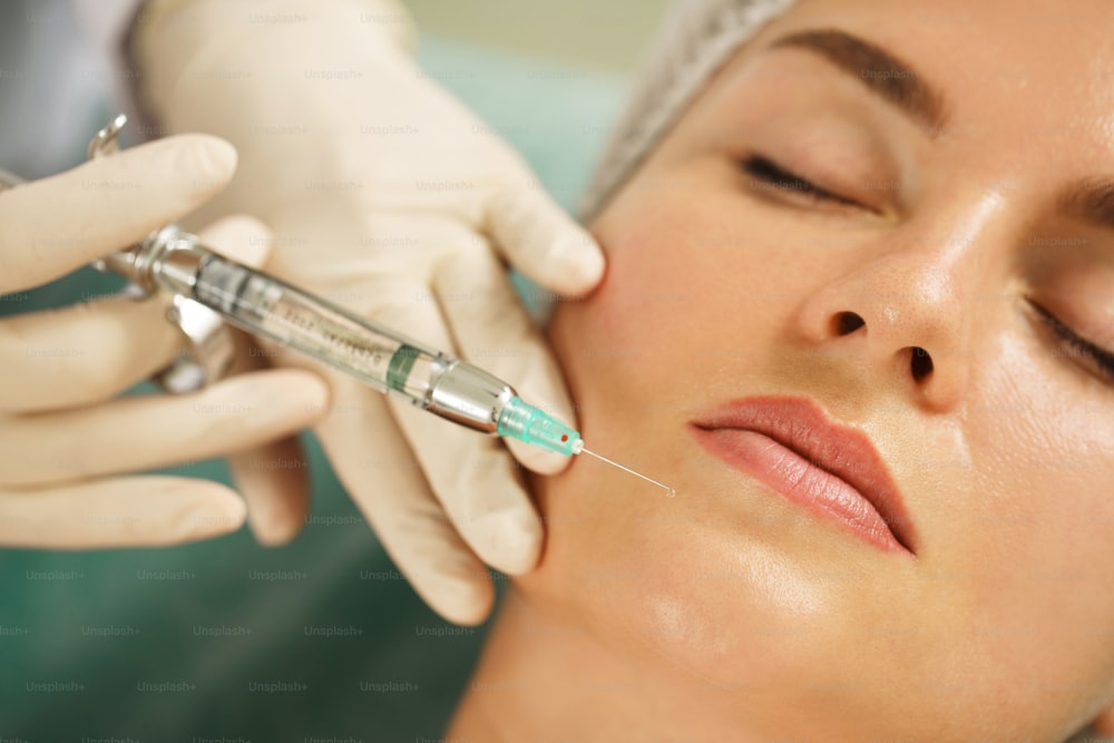 美容クリニックで顔面手術前に局所麻酔薬の注射を受ける女性クライアント