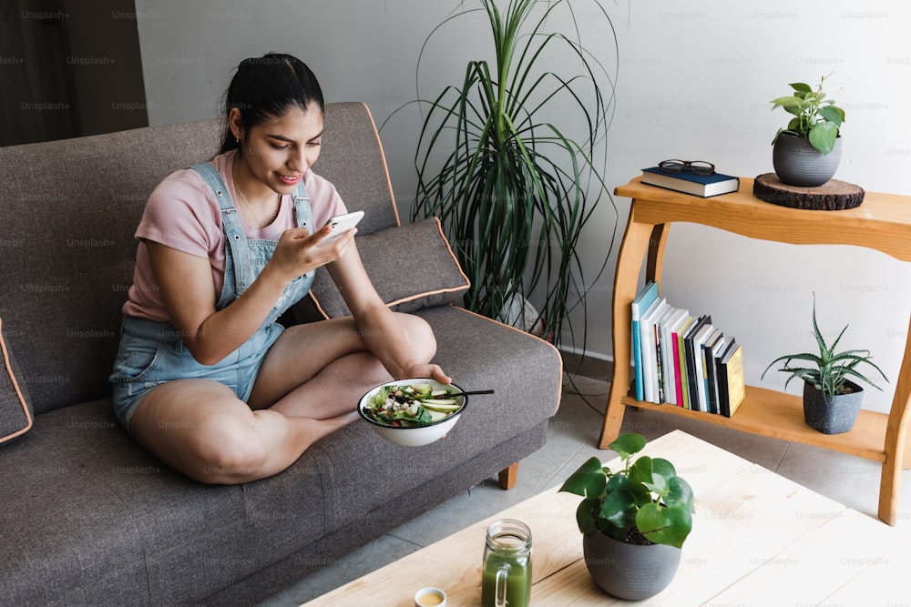 jeune femme latine mangeant des légumes ou un saladier tout en prenant une photo avec un téléphone portable à la maison au Mexique Amérique latine