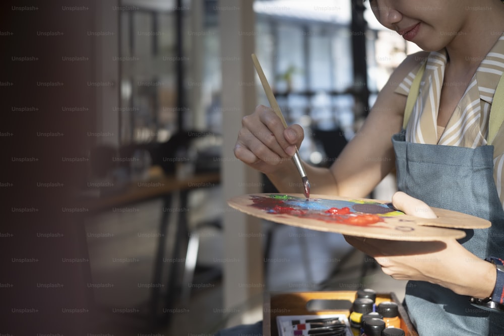 Artista femenina de tiro recortado sosteniendo un pincel y mezclando pintura al óleo de color en la paleta.