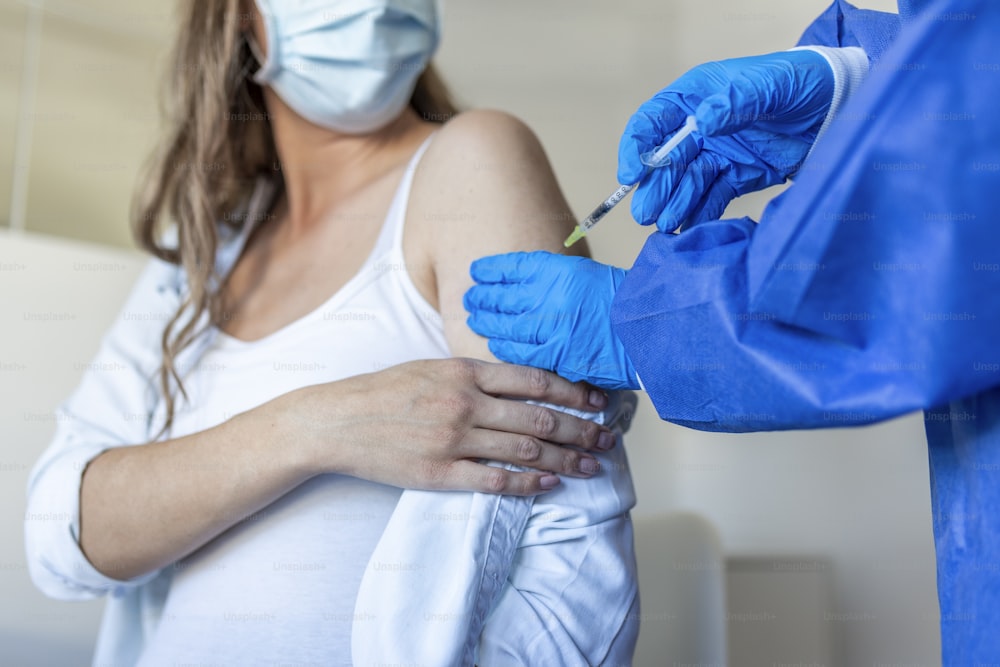 Doctora administrando la inyección de la vacuna contra el Covid-19 a una joven embarazada en un centro de salud. Mujer embarazada siendo inmunizada contra el coronavirus en la clínica. Concepto de vacunación de la población