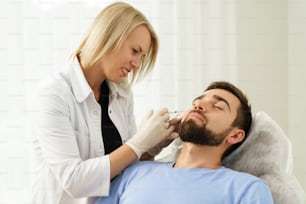 Médico femenino y cliente masculino durante las inyecciones de relleno en una clínica de medicina estética