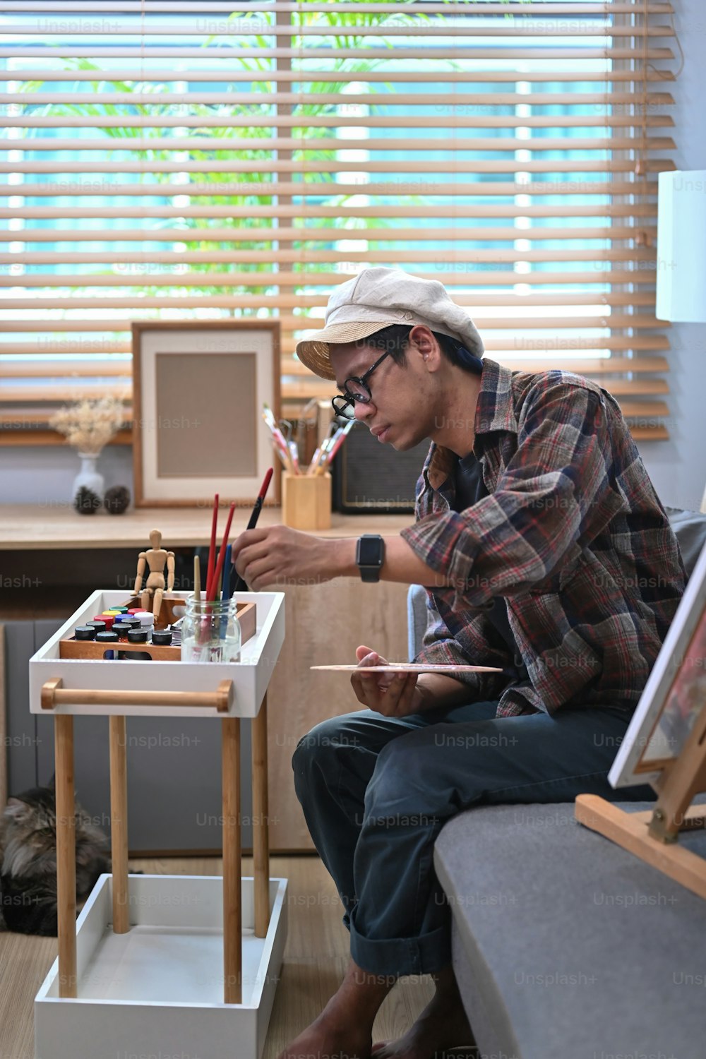 Junger asiatischer Mann malt Bild mit Aquarell im Wohnzimmer.