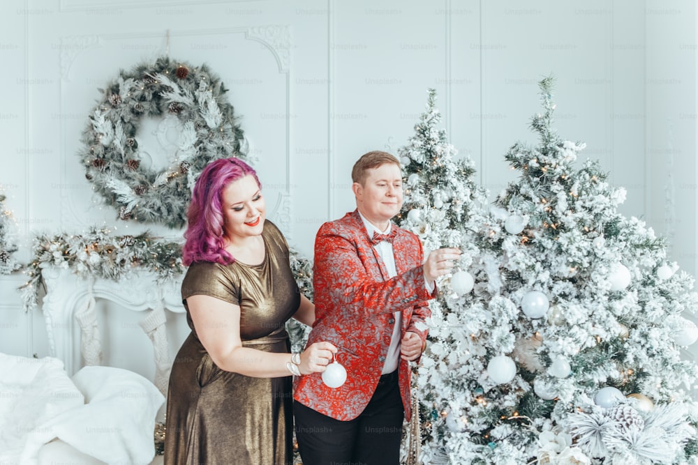 LGBTQ lesbian couple celebrating Christmas or New Year winter holiday together. Gay female lady with butch partner decorating Christmas tree at home. Winter holiday mood spirit.