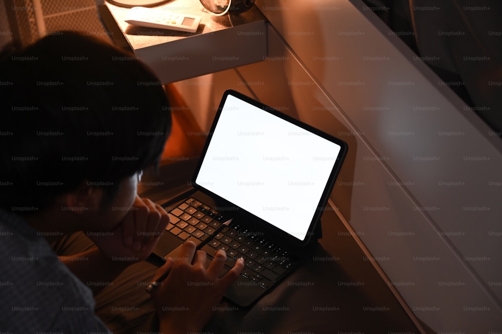 Homem navegando na internet com mesa de computador à noite no quarto.