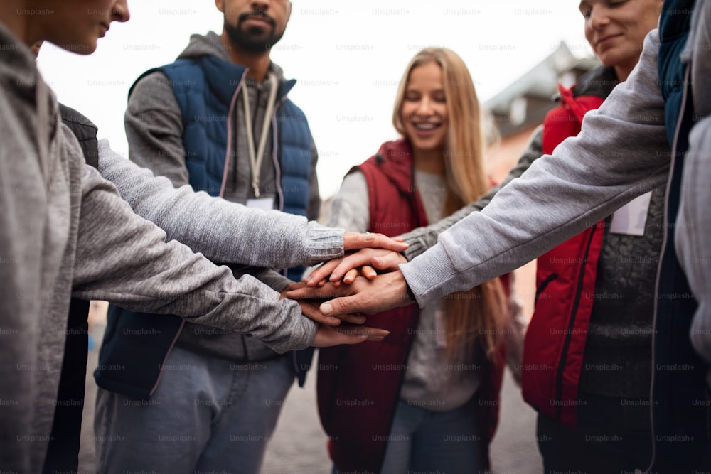 Un gros plan d’un groupe de bénévoles heureux du service communautaire empilant les mains ensemble à l’extérieur dans la rue