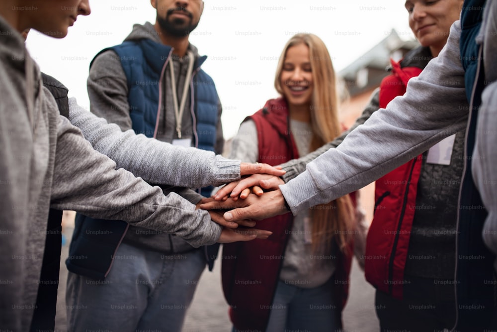 Un primer plano de un grupo de voluntarios felices del servicio comunitario apilando las manos juntas al aire libre en la calle
