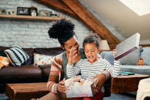 Excited African American daughter opening gift box she received from her mother at home.