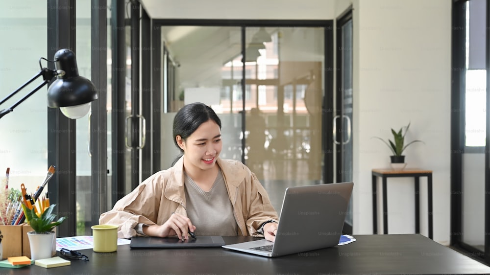 Designer donna asiatica che lavora con laptop in ufficio creativo.