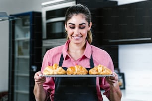 young Latin woman baking croissant on oven in kitchen in Mexico Latin America