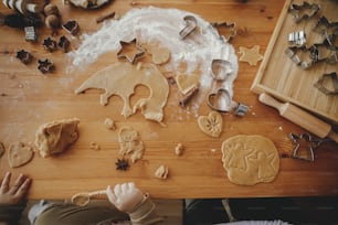Family making together christmas cookies on messy table, top view. Atmospheric holiday time. Cute daughter and mother cutting dough for gingerbread cookies. Authentic moments