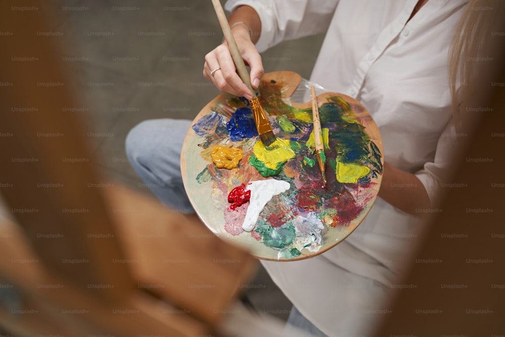 Relaxed female person sitting opposite easel while drawing picture on masterclass